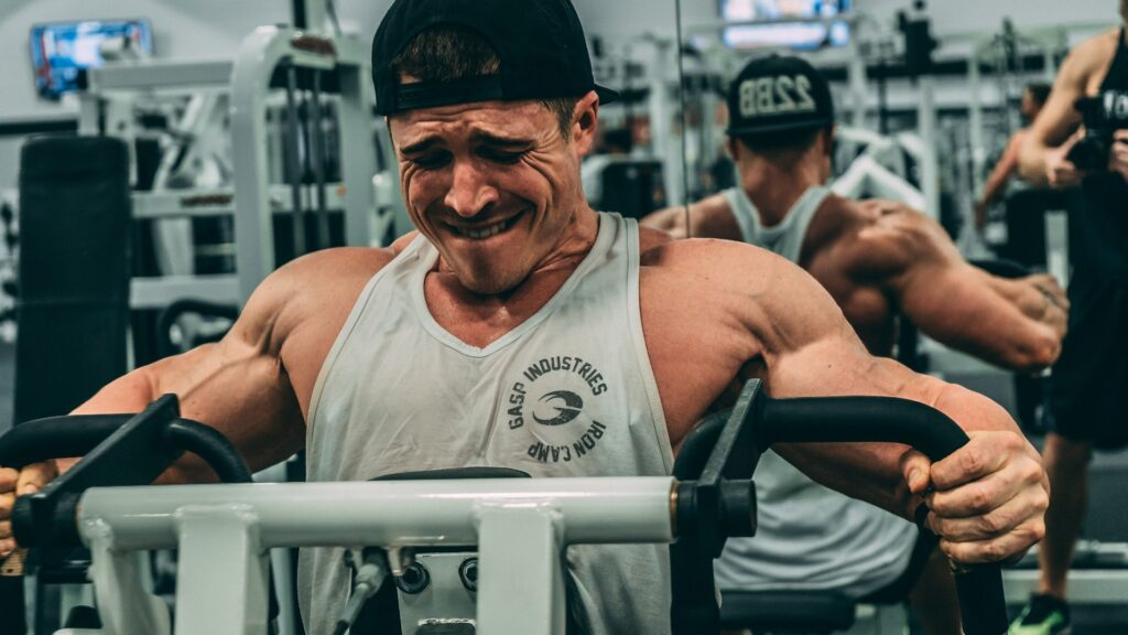 A man training a horizontal row on a machine at the gym, grimacing due to his training intensity