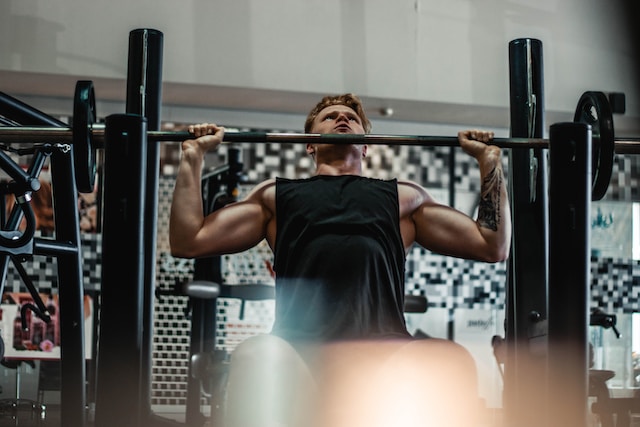 A man sat down at the gym showing his exercise set up for a vertical pressing movement with a barbell