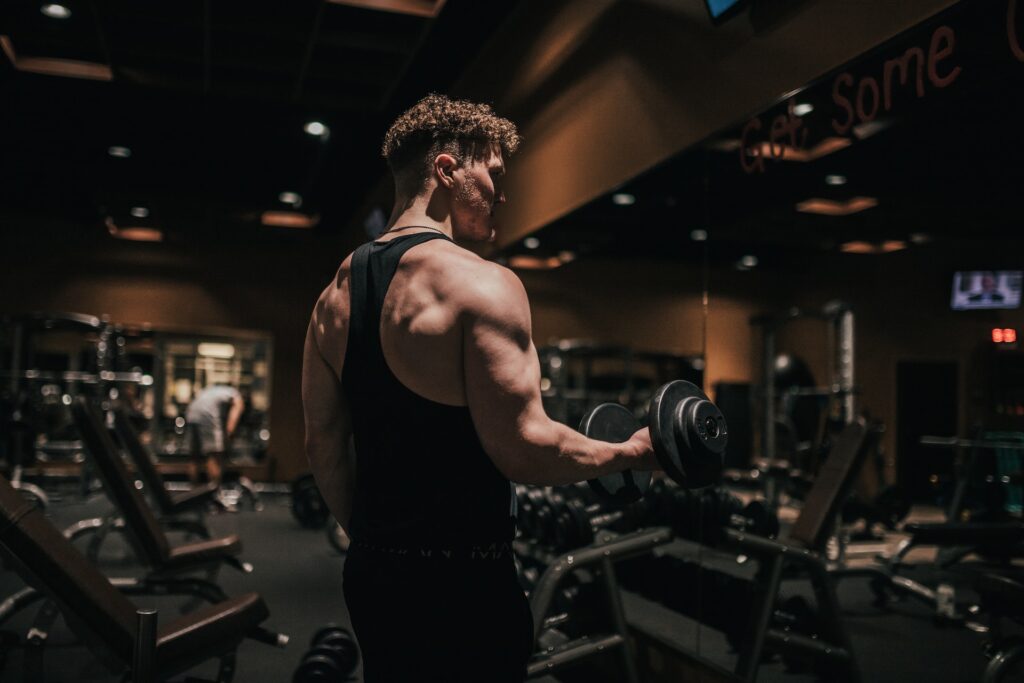 A man stood in a dark gym slowly bicep curling a dumbell showing good eccentric rep speed